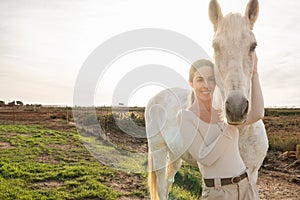 Young happy equestrian female posing and having fun with her horse near a farm