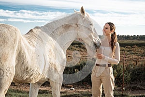 Young happy equestrian female posing and having fun with her horse near a farm