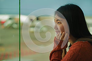 Young happy and excited Asian Chinese student woman with backpack at airport departure lounge watching aircraft through glass