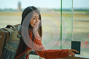 Young happy and excited Asian Japanese student woman with backpack at airport departure lounge watching aircraft through glass