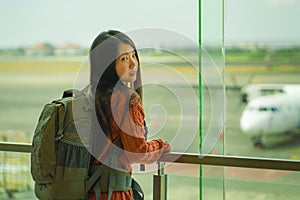 Young happy and excited Asian Korean student woman with backpack at airport departure lounge watching aircraft through glass