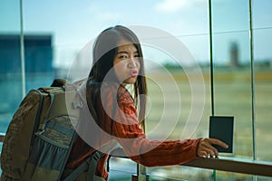 Young happy and excited Asian Korean student woman with backpack at airport departure lounge watching aircraft through glass