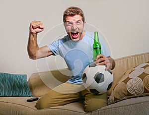 Young happy excited and crazy football fan man holding soccer ball celebrating team scoring goal and victory watching game on tele