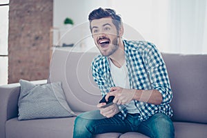 Young happy excited man sitting on sofa holding joypad and playing video games and having fun