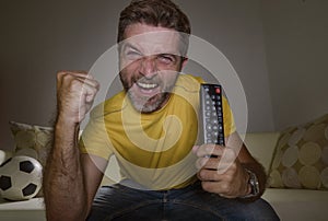 Young happy and excited man watching European football game on TV celebrating goal on couch screaming spastic gesturing crazy