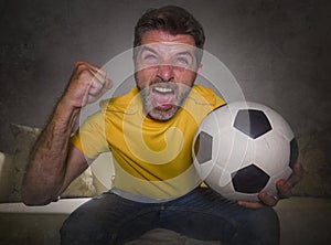 Young happy and excited man watching European football game on TV celebrating goal on couch screaming spastic gesturing crazy