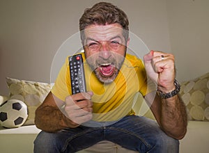 Young happy and excited man watching European football game on TV celebrating goal on couch screaming spastic gesturing crazy