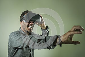 Young happy and excited man wearing virtual reality VR goggles headset experimenting 3d illusion playing video game touching