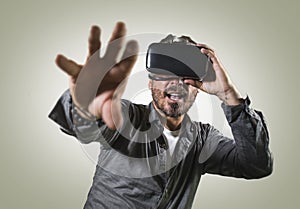 Young happy and excited man wearing virtual reality VR goggles headset experimenting 3d illusion playing video game touching