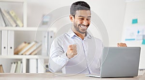 Young happy and excited mixed race businessman cheering in support while working on a laptop alone in an office at work