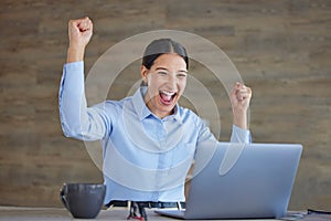 Young happy and excited mixed race businesswoman cheering with her fists working on a laptop sitting in an office at