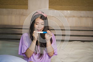 Young happy excited pregnant Asian Japanese woman at home holding predictor and checking positive result on pregnancy test feeling