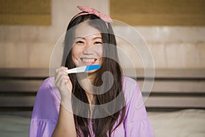 Young happy excited pregnant Asian Korean woman at home holding predictor and checking positive result on pregnancy test feeling b