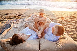 Young happy family on the beach at sunset lie on a blanket