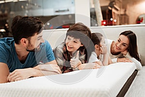 Young happy family checks on softness of orthopedic mattress, lying on bed in furniture store.