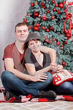 Young and happy family couple sitting near decorated New Year tree. Closeup portrait.