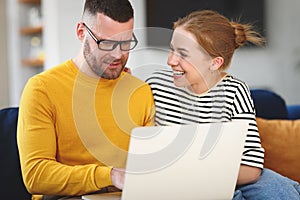 Young happy family couple using laptop while sitting on sofa at home
