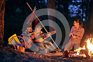 A young happy family enjoying a guitar and a campfire in the forest photo