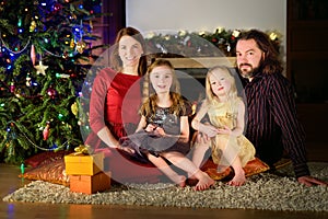 Young happy family of four sitting by a fireplace on Christmas eve