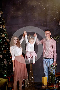 Young happy family with little baby girl in cozy home interior with festive Christmas tree. Good mood and having fun