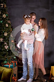 Young happy family with little baby girl in cozy home interior with festive Christmas tree. Good mood and having fun