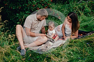 Young happy family with little beautiful baby with blue eyes walking in summer park at sunset.