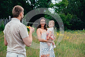 Young happy family with little beautiful baby with blue eyes walking in summer park at sunset.