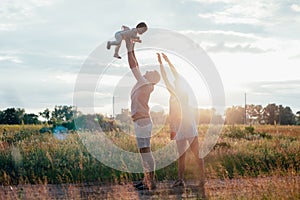 Young happy family with little beautiful baby with blue eyes walking in summer park at sunset.