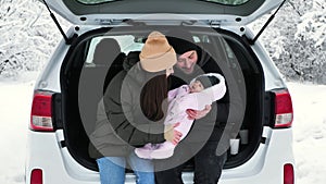 Young, happy family: a man, a woman and a baby are sitting in the trunk of a car
