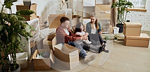 Young happy family, man, woman and kid sittin on floor in new living room. Moving into new flat, apartment with many