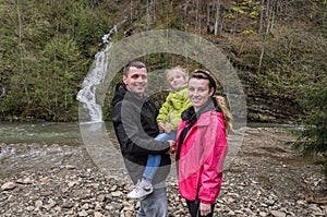 Young happy family: mom, dad and daughter on the background of a mountain waterfall