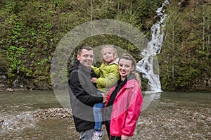 Young happy family: mom, dad and daughter on the background of a mountain waterfall