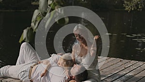 Young happy family mom father and son on the pier near the river on a sunny day. A man lies on a woman lap