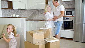 Young happy family moving to new apartment. Two little girls running into new home with parents at background cardboard