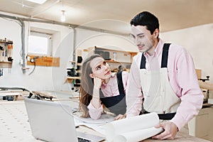 Young happy family standing at a work bench in a carpentry workshop, writing a project. Family business. startup business. young