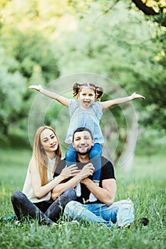 Young happy family of three having fun together outdoor. Pretty little daughter on her father piggyback smiling and have fun.