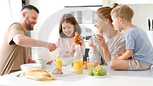 Young happy family with two cute little kids having breakfast together in kitchen and smiling