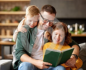 Young happy family with two kids reading book together while spending leisure time at home