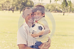 Young happy father carrying on his back excited 7 or 8 years old son playing together soccer football on city park garden posing s