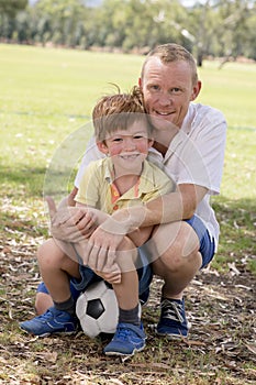 Young happy father and excited 7 or 8 years old son playing together soccer football on city park garden posing sweet and loving h