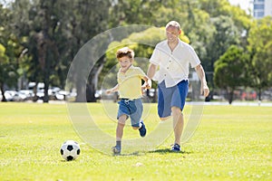 Young happy father and excited little 7 or 8 years old son playing together soccer football on city park garden running on grass k