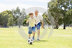 Young happy father and excited little 7 or 8 years old son playing together soccer football on city park garden running on grass k