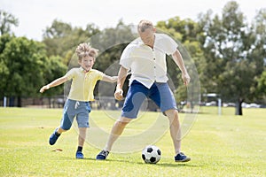 Young happy father and excited little 7 or 8 years old son playing together soccer football on city park garden running on grass k