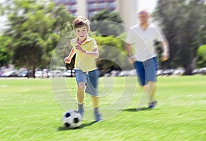 Young happy father and excited 7 or 8 years old son playing together soccer football on city park garden running on grass kicking
