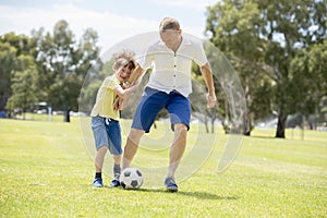 Young happy father and excited little 7 or 8 years old son playing together soccer football on city park garden running on grass k