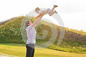 Young happy father holding baby son in hands over his head outdoors