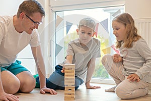 Young happy father playing with his two cute children with wooden blocks