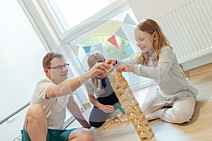 Young happy father playing with his two cute children with wooden blocks