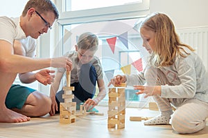 Young happy father playing with his two cute children with wooden blocks