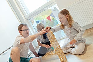 Young happy father playing with his two cute children with wooden blocks